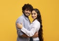 Happy young indian spouses. Portrait of cheerful couple hugging and smiling at camera, standing over yellow background Royalty Free Stock Photo