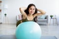 Happy young Indian woman doing exercises with fitness ball, strengthening her back muscles at home Royalty Free Stock Photo