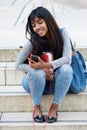 Happy young Indian woman sitting on steps with mobile phone Royalty Free Stock Photo