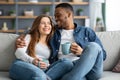 Happy Young Interracial Couple Drinking Coffee And Hugging On Couch At Home Royalty Free Stock Photo