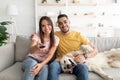 Happy young interracial couple sitting on couch with their funny dog and watching TV at home Royalty Free Stock Photo