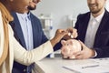 Young couple put money in piggy bank sitting at desk with broker or financial advisor Royalty Free Stock Photo