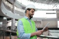 Happy young islamic builder engineer with beard in protective clothing and hard hat typing on tablet