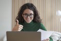 Happy young Italian female employee talks online on laptop with colleagues and showing thumb up