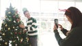 Happy young joyful Asian couple having fun taking photos, decorating various baubles on the Christmas tree in the living room. Royalty Free Stock Photo