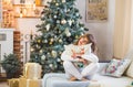 Happy young lady with curly hair sits near the Christmas tree