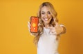 Young lady pointing at mobile phone with smarthome app on screen, regulating temperature over orange background, collage