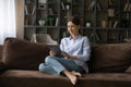 Happy young lady rest on comfy sofa holding digital tablet