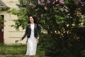 Happy young lady walking on the street near the bloomy lilac tree on the summer day