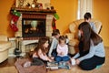 Happy young large family by a fireplace in warm living room on winter day. Mother with four kids at home read book