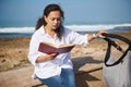 Happy young Hispanic woman, mother pushing baby stroller, reading book, sitting relaxed on the parapet on Atlantic beach Royalty Free Stock Photo