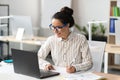 Happy young latin businesswoman working in office, sitting at workplace, using modern computer and taking notes Royalty Free Stock Photo