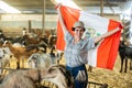 Happy young Latin female traveler waving Peruvian flag during visit to livestock goat farm