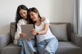 Happy young lesbian couple hugging having fun using digital tablet relaxing on couch at home. Two smiling asian women Royalty Free Stock Photo