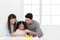 Happy young little asian cute girl watching or playing digital tablet, laptop or mobile with cheerful parents on desk in family