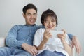 Happy young love asian couple sitting on couch at home, looking at mobile phone, Asian teen couples are enjoying the game Royalty Free Stock Photo