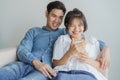 Happy young love Asian couple sitting on couch at home, looking at mobile phone, Young asian people are using smartphone Royalty Free Stock Photo