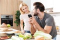 Happy young loving couple cooking together using phone Royalty Free Stock Photo