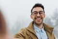 Happy young male is making self portrait on a camera outdoors. Handsome young man in coat and blue shirt wear eyeglasses making Royalty Free Stock Photo