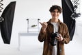 Happy young male photographer working at modern photostudio, pointing to the side, enjoying making content photoshoot
