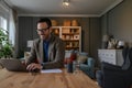 Happy young male professional in elegant suit typing e-mail over laptop on desk in home office