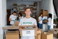 Happy young male volunteer in uniform holding box for donation, team working together in charitable organization office Royalty Free Stock Photo