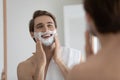 Happy young man applying shaving foam on face. Royalty Free Stock Photo