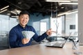 Happy young man Asian businessman sitting in the office at the table holding cash money in his hands Royalty Free Stock Photo
