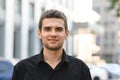 Happy young man in black shirt on urban background looking into camera and smiling. Closeup portrait of handsome guy in dark shirt Royalty Free Stock Photo