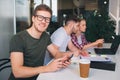 Happy young man in black short look on camera adn sile. He sit with his colleagues in white coom. Guy hold phone in Royalty Free Stock Photo