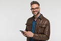 Happy young man in brown leather jacker holding telephone and smiling Royalty Free Stock Photo