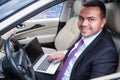 Happy young man in business suit sits in driver`s seat in car with laptop. Working with a laptop in the car