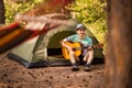 Happy young man camping and strum a guitar instrumental music to relax against background of forest sunset. Wilderness Travel Royalty Free Stock Photo