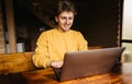 Happy young man in casual clothes sitting at a wooden table in the country and working on a laptop. Work on the Internet with a Royalty Free Stock Photo