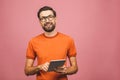 Happy young man in casual standing and using tablet isolated over pink background