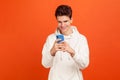 Happy young man in casual style hoodie holding cellphone and smiling looking at screen, teenager using entertainment app, Royalty Free Stock Photo