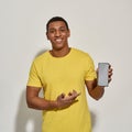 Happy young man in casual yellow t shirt smiling at camera, showing and pointing at smartphone with blank screen while Royalty Free Stock Photo