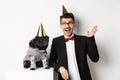 Happy young man and cute black dog wearing party cones, celebrating birthday, guy friendly saying hello and waving hand Royalty Free Stock Photo