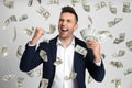 Happy young man with dollars under money rain on background