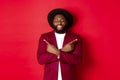 Happy young man dreaming and pointing fingers sideways, close eyes and smiling, showing two things, standing over red Royalty Free Stock Photo