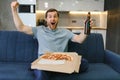 Happy young man drinking beer and eating pizza when watching game on tv at home Royalty Free Stock Photo