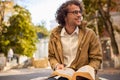 Happy young man with glasses reading and posing with book outdoors. College male student carrying books in campus in autumn street Royalty Free Stock Photo