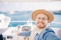 Happy young man in hat goes on trip on white yacht sea making selfie photo on camera, concept travel life hipster Royalty Free Stock Photo