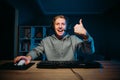 Happy young man in headset playing video games at home on computer and streaming on internet, looking at camera and showing thumbs Royalty Free Stock Photo