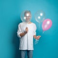 Happy young man hiding his face behind balloon against colorful blue studio wall background Royalty Free Stock Photo