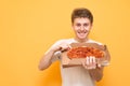 Happy young man holding a box of fresh pizza from the delivery, looking into the camera and smiling, isolated. Portrait of a Royalty Free Stock Photo