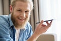 Happy young man holding phone using virtual voice assistant looking at camera.