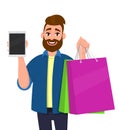 Happy young man holding shopping bags. Person showing blank screen tablet computer in hand. Male character illustration. Royalty Free Stock Photo