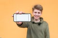 Happy young man holding a smartphone with a white screen on an orange background and smiling Royalty Free Stock Photo