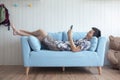 Happy young man lying on couch playing tablet at home in living room Royalty Free Stock Photo